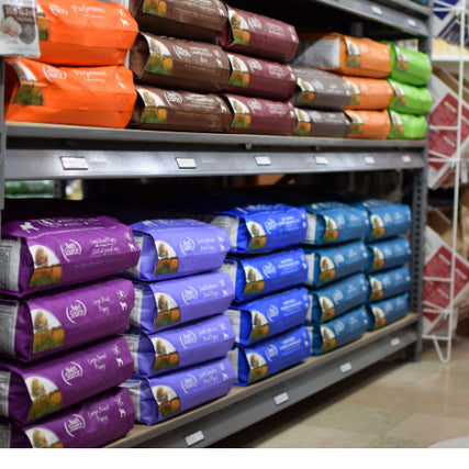 Pet Food & SuppliesShelves filled with colorful dog food bags in a pet store. Varied packaging in orange, brown, green, purple, blue, and teal. Tidy, organized display.